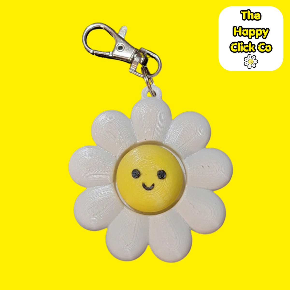 A white daisy shaped  fidget clicker keychain with a smiling yellow face in the center and a silver clasp at the top, shown on a bright yellow background. A 'The Happy Click Co' logo is visible in the top right corner.