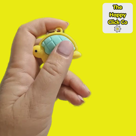 A clicking video of a yellow turtle-shaped fidget clicker keychain with a mint green shell, attached to a silver metal clasp, shown against a bright yellow background with a 'The Happy Click Co' logo in the top right corner.